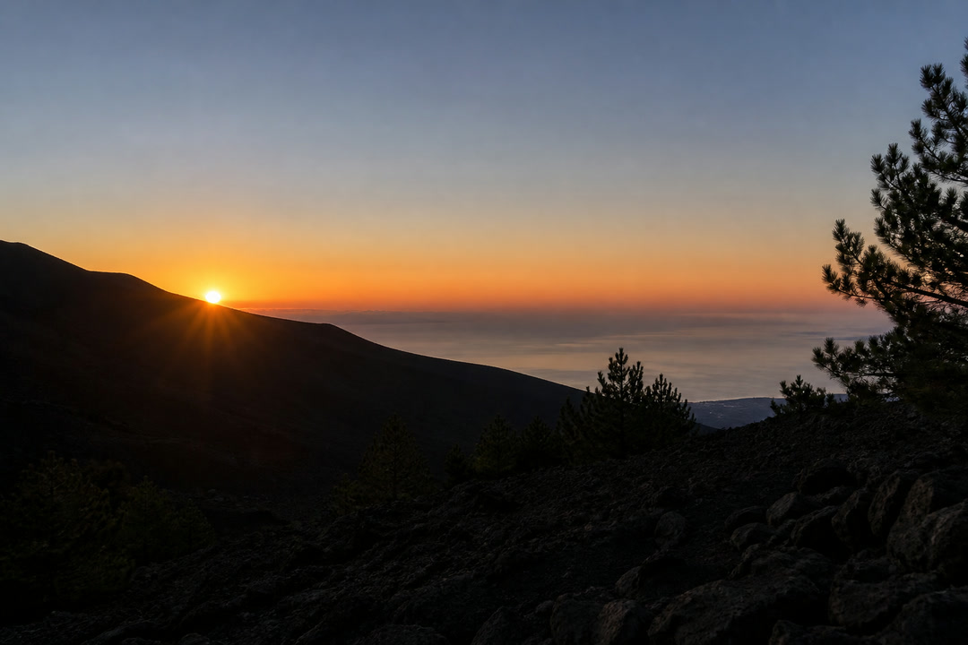 Il sole che sorge dietro il profilo del vulcano con il mare sullo sfondo
