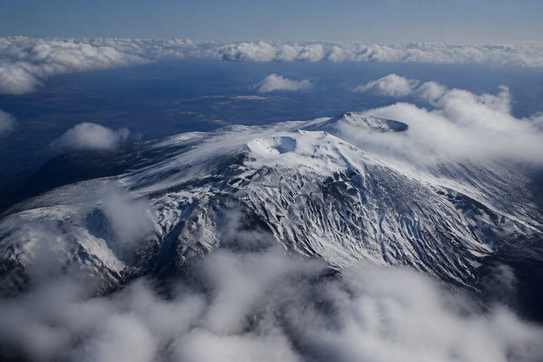 L’Etna innevato visto dall’alto, in volo tra le nuvole