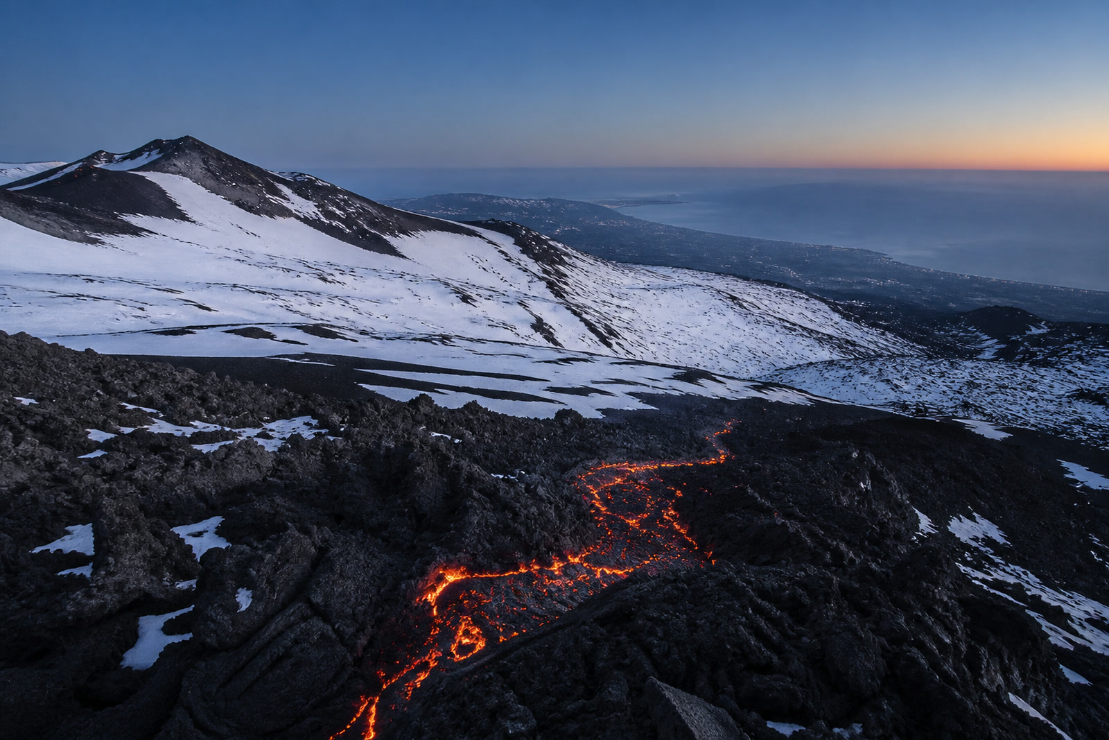 La colata incandescente tra le sciare innevate, con la costa sullo sfondo