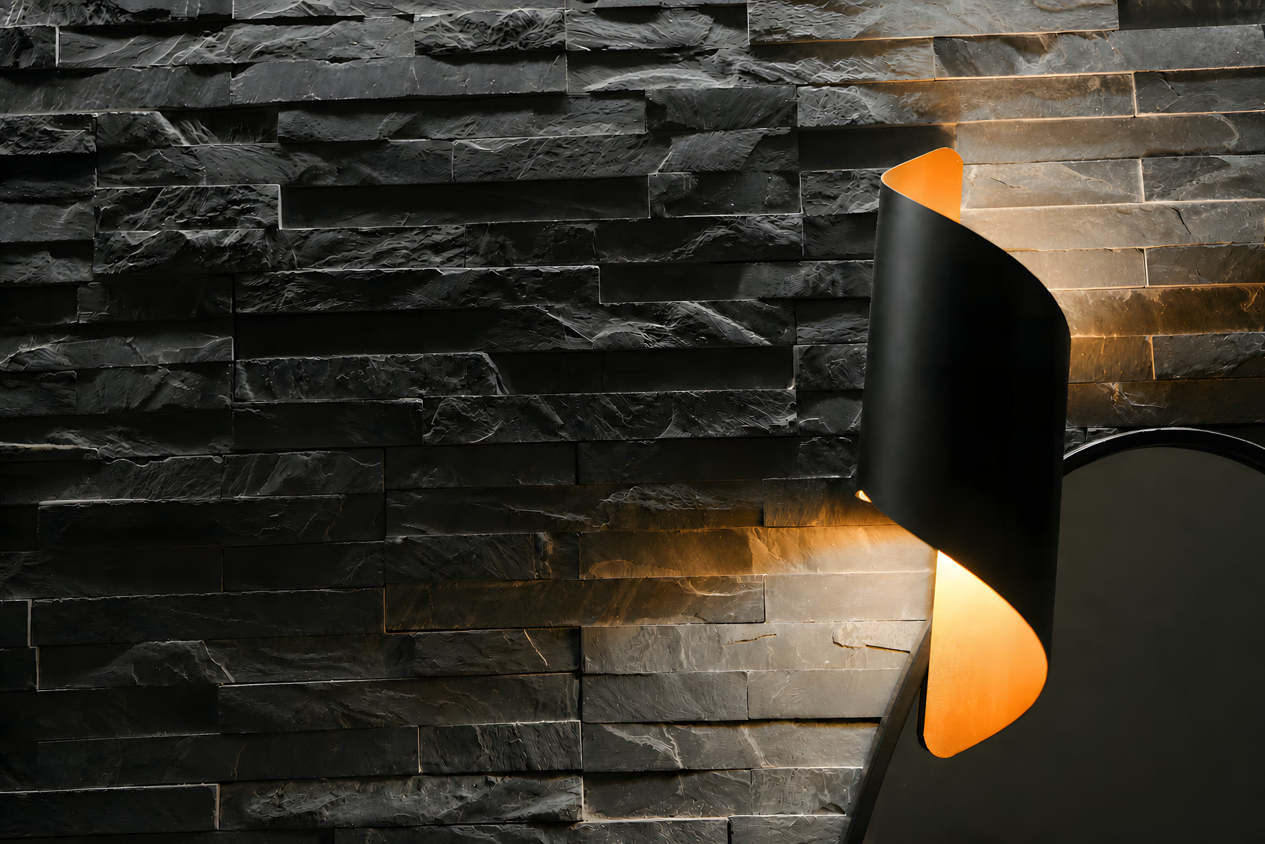 Parete in pietra lavica nera illuminata da un'applique nera e oro