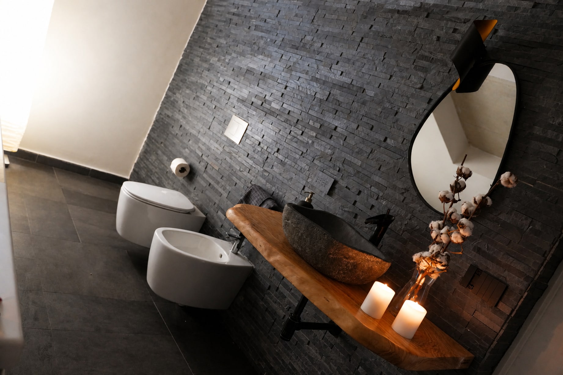 Il bagno della suite: lavabo in pietra su mensola di legno massello, specchio sagomato e parete in pietra nera