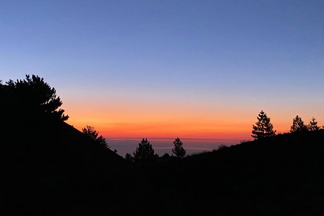 Il sole che sorge dietro il profilo del vulcano con il mare sullo sfondo