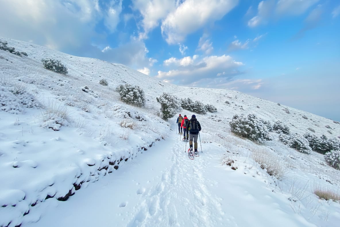 Ciaspolatori in fila sulla neve con la Valle del Bove alle spalle