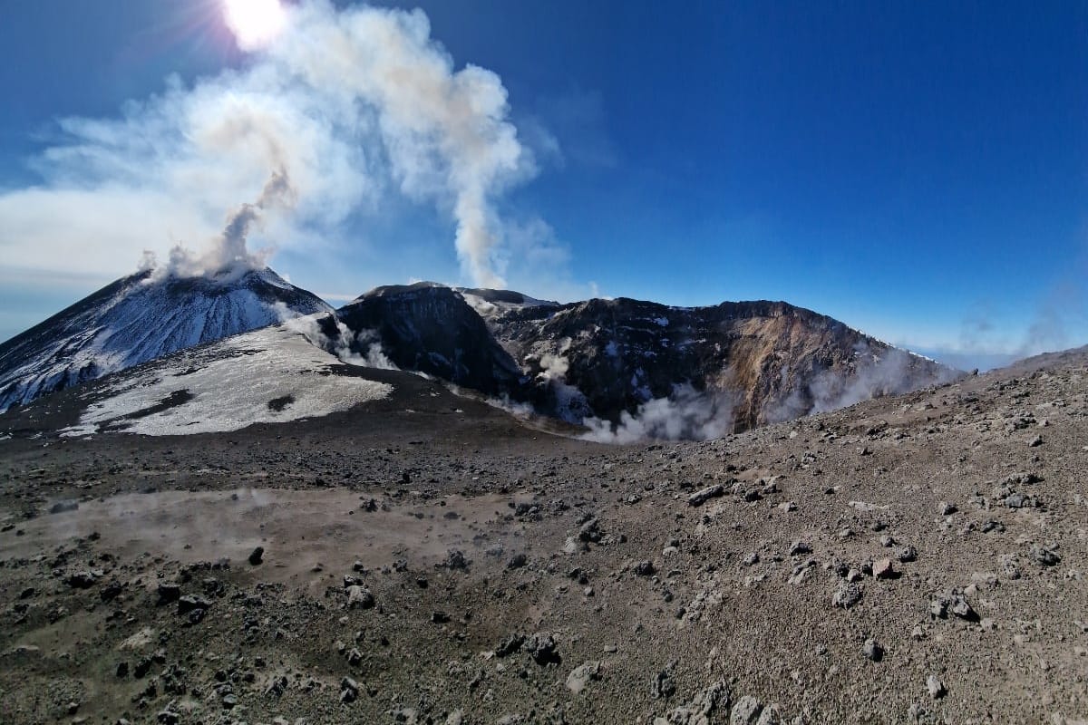I crateri sommitali innevati che fumano contro il cielo blu