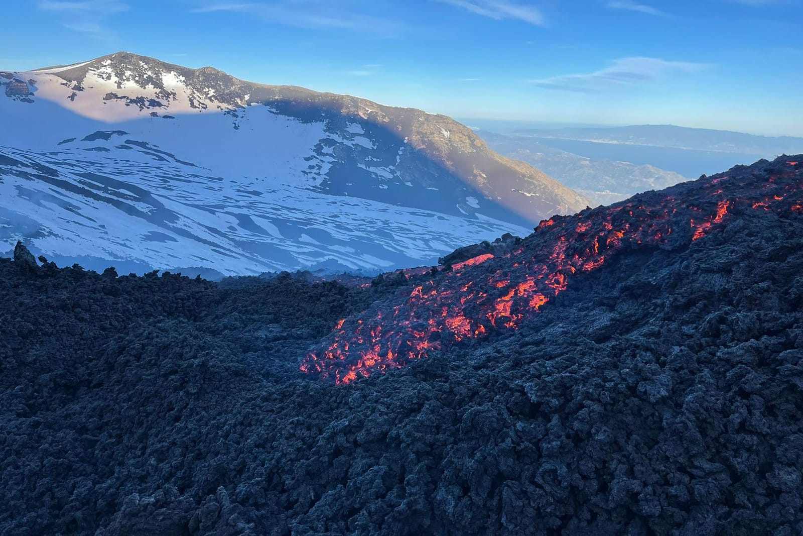 La colata incandescente tra le sciare innevate, con la costa sullo sfondo