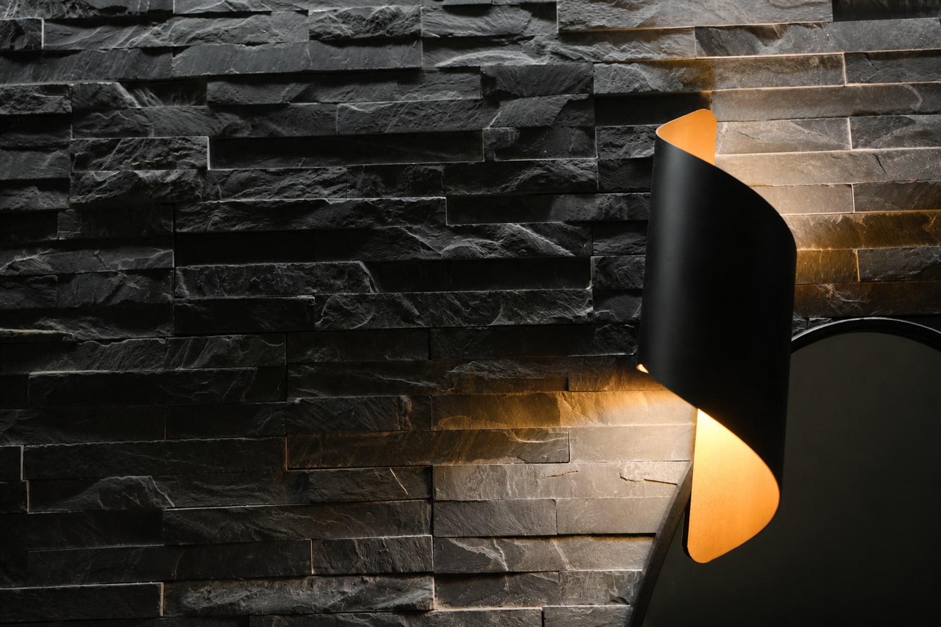 Parete in pietra lavica nera illuminata da un'applique nera e oro